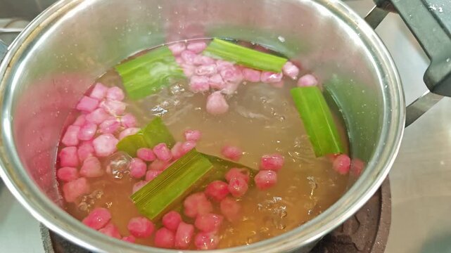 Traditional Thai dessert preparation, sweet red ruby water chestnuts simmering in hot syrup with aromatic pandan.