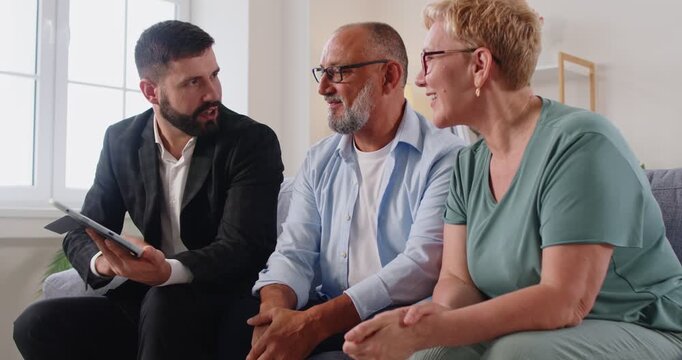 Reak estate agent consults a senior couple at home. Advisor covers finance and retirement planning in a clear consultation, using a tablet to outline options and contract points during a meeting.