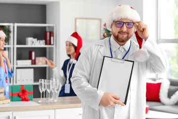 Male doctor in Santa hat with clipboard at hospital on Christmas eve