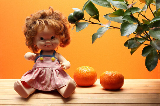 Close-up photo with sitting good doll and tangerines. Photo with deep depth of field on orange background.