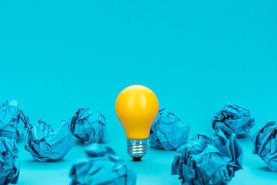 Great idea concept with bulb and crumpled office paper. Concept of inspiration, idea generation and problem solving. Conceptual photo of light bulb standing on turquoise blue background.