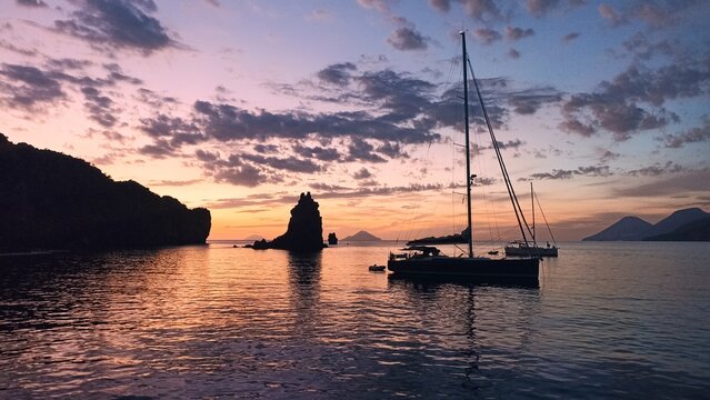 Sailboats anchored at sunset beside dramatic volcanic rock stack, Lipari, Aeolian Islands, Sicily, Italy