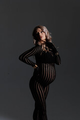 Fototapeta premium Dramatic studio portrait of a pregnant woman posing in a form-fitting black lace bodysuit that accentuates her baby bump. With a confident and expressive pose, she raises her arm to her forehead, crea