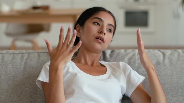 Frustrated Indian Arabian woman at home couch suffering high temperature broken air conditioner sweating female feeling summer heat hormonal health problem medicine indoors stress ventilation issue