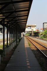 Fototapeta premium Empty train station platform with tracks stretching into the distance under a shelter