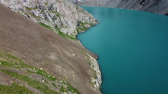 Aerial view of a vertical divide between a steep rocky cliff and a calm turquoise lake, metaphor for balance, risk, and the human path between two worlds.