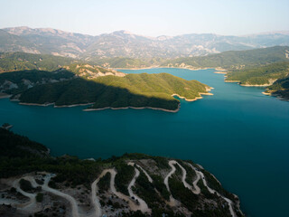 Obraz premium Aerial view of Bovilla Lake with winding mountain road and turquoise water surrounded by green hills near Tirana, Albania in soft sunlight