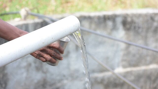 An empty glass in hand filling water from well pipe