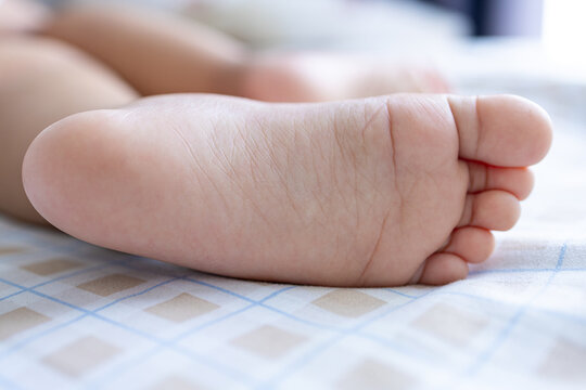 Close-up of a Cute Baby Foot on a Bed,A detailed close-up shot showing the soft, wrinkled skin and tiny toes of a newborn baby's foot resting on a checkered blanket. The image conveys themes.