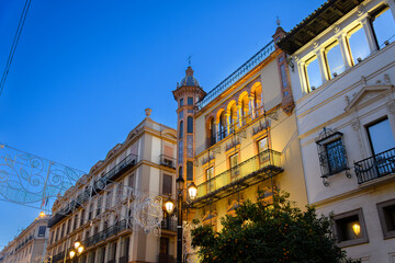 Obraz premium Evening view of the illuminated Casa de Álvaro Dávila, Marquis of Villamarta, a historic building featuring ornate wrought iron balconies and Adalusian architecture in downtown Seville, Spain.