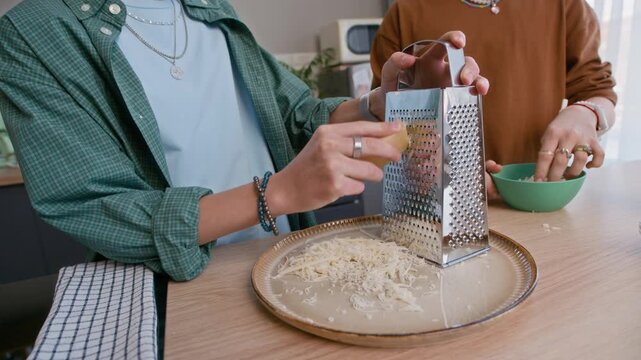 Tilt down shot of Caucasian teen couple grating cheese together in bright kitchen interior