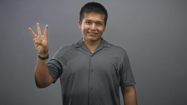Man showing progressive finger count with left hand and wristwatch, wearing gray shirt against a gray studio backdrop; friendly counting lesson.