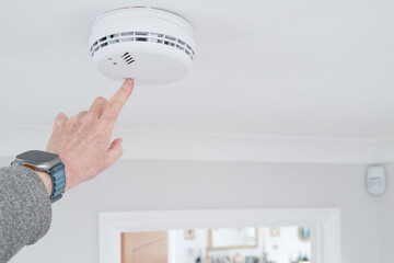 Handyman seen doing a weekly test of a combine smoke and carbon monoxide tester in a home hallway. The detector is wired into the house wiring a requires no battery. © Nick Beer