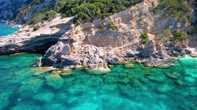 Cala Mariolu Sardinia 4k drone follow video of motorboat on turquoise water and huge rocks. Scenic Orosei gulf view of transparent sea and majestic limestone cliff in Italy. Mediterranean sea b-roll