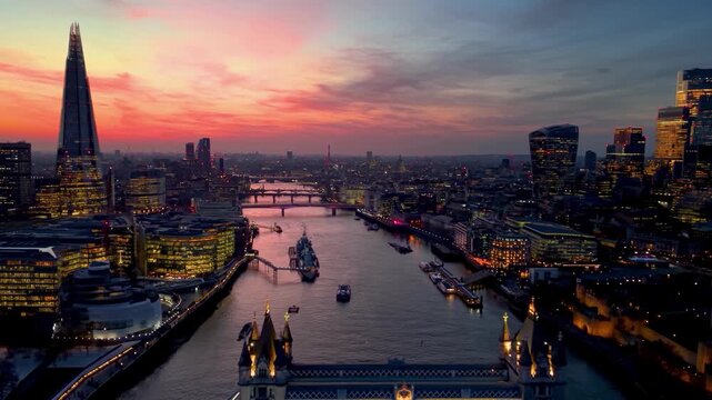 Establishing aerial view towards the Tower Bridge in London, England, with city skyline and river Thames during dusk with a colorful sky