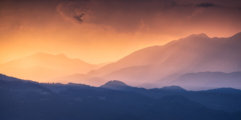 Naklejka premium Silhouettes of Alpine mountains at colorful sunset in summer in Slovenia. Landscape with mountain ridges in fog, golden sunlight and clouds in the evening. Alps. Nature. Hills in sunlight. Scenery