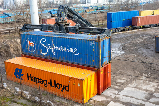 WARSAW, MASOVIAN, POLAND - FEBRUARY 27 2026: A heavy reach stacker maneuvers a blue Safmarine shipping container at a busy industrial logistics terminal.