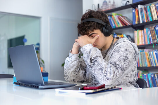 Overwhelmed high school student struggling to focus on studies, feeling fatigue and procrastination, sitting at desk with bookshelves in the background, mental health concept, ADHD management
