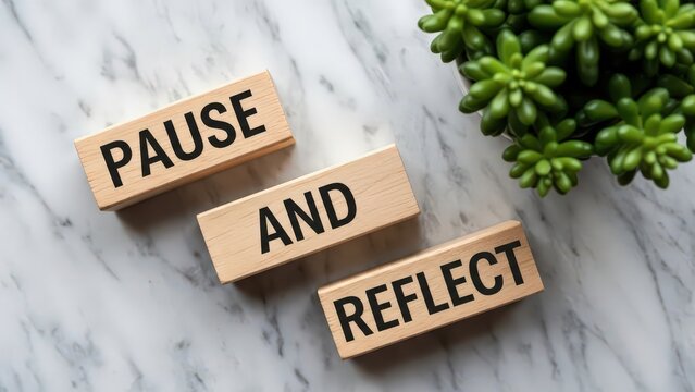 Wooden blocks with the words pause and reflect on a marble background with a succulent plant
