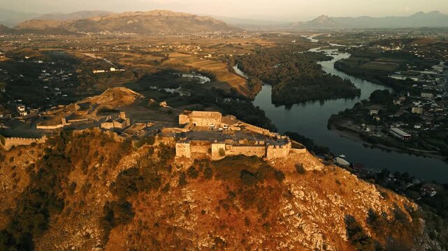 Aerial Forward Flight Over Rozafa Castle in Shkodra, Albania at Golden Hour with River Bends and Mountain Panorama in Background