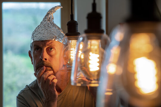 Tinfoil hat picture. A man wearing a tinfoil hat looks at his laptop with a worried look on his face. Paranoia and conspiracy theory. Alien abduction and government cover up. Mind control and brainwas