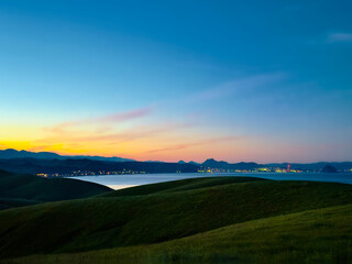 Fototapeta premium View of sunset, sunrise, over hills and ocean and coastline, and city lights