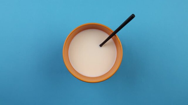 Travelling en plong&eacute;e verticale d'un bol de lait en rotation sur fond bleu uni