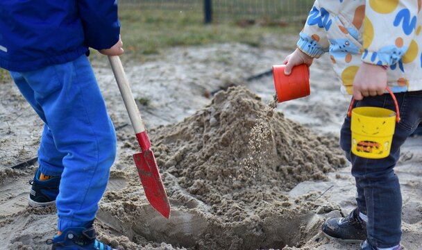 Children boy and girl playing together in sandbox digging sand with shovel and bucket, teamwork and interaction, outdoor playground activity, natural lifestyle moment