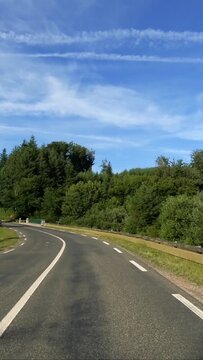 Curved asphalt road winding through lush green forest under a blue sky in the Morvan region of France. Peaceful rural landscape ideal for travel and nature concepts.
