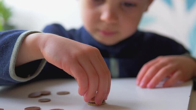Child's Hand Reaching for Coins Scattered on Table Surface &mdash; Low Angle View, Child Financial Literacy, Counting Money and Early Numeracy Concept