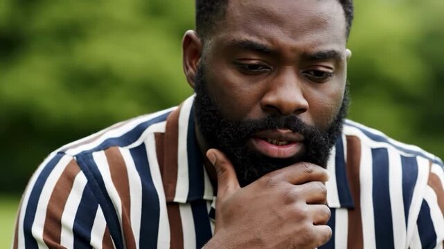 A man with a beard covering his face with his hand outdoors