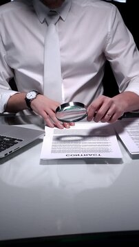 Business person examining a document using a magnifying glass, focusing on fine print and terms in a legal agreement, working late. Audit and overworking concepts
