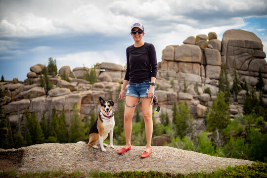 A tricolor dog outside with a woman in shorts and a hat