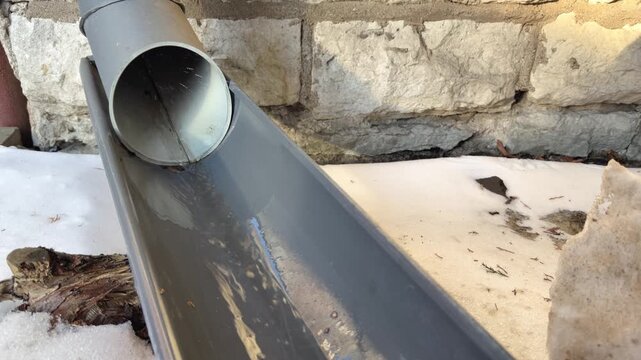 Rainwater flowing along gutter from roof drain pipe exterior building close up