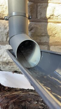 Water flowing from roof drain pipe into gutter close up exterior building detail