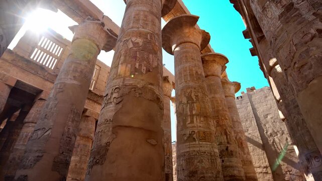 Great Hypostyle Hall at Karnak Temple, Luxor Egypt. Massive painted columns with original red hieroglyphics soaring against bright blue sky. Iconic ancient architecture.
