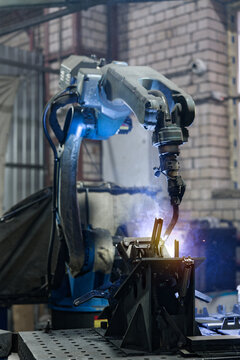 Industrial robot performing arc welding on metal detail in factory