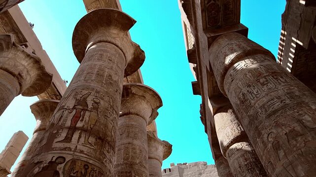 Great Hypostyle Hall at Karnak Temple, Luxor Egypt. Massive painted columns with original red hieroglyphics soaring against bright blue sky. Iconic ancient architecture.