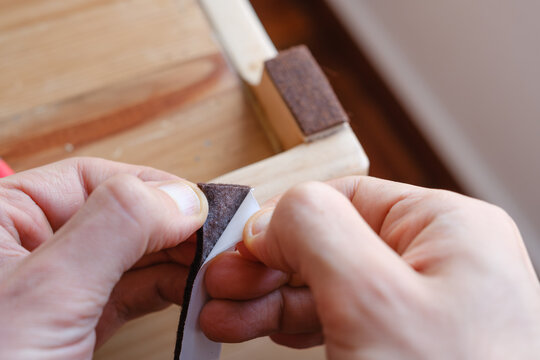Hands applying adhesive felt furniture pads protecting wooden floor