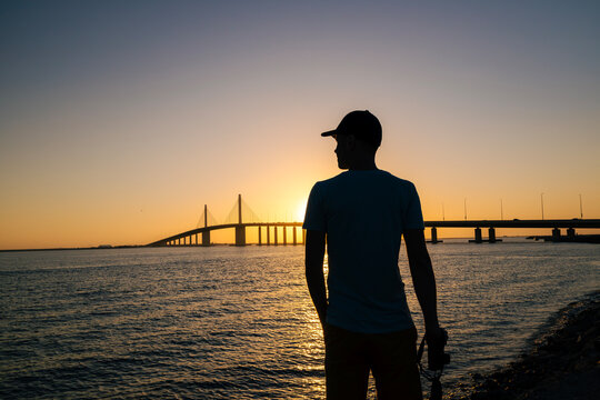 Silhouette tourist standing on Al Bateen Beach in Abu Dhabi, United Arab Emirates, watching sunset over Arabian Gulf. Calm evening atmosphere, travel and leisure concept.