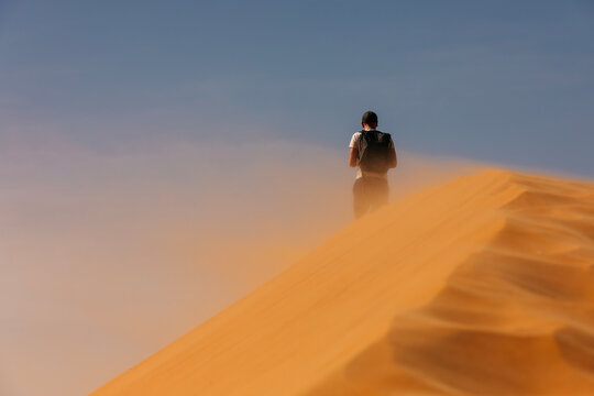 Tourist with backpack standing on sand dune in Abu Dhabi desert, feeling wind. Desert landscape, adventure, travel, and outdoor exploration concept.