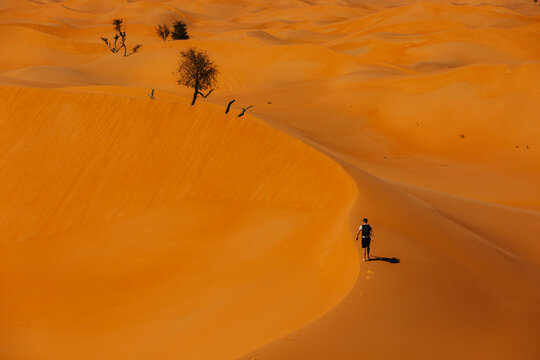 Tourist with backpack walking on sand dune in Abu Dhabi desert. Desert landscape, adventure, travel, and outdoor exploration concept.
