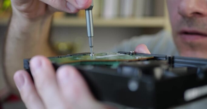Man repairs hard drive with precision tools. Focused technician demonstrates skills in technology maintenance. small business. Close-up shows intricate process of fixing computer hardware components.