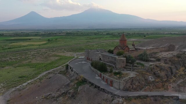 Aerial drone footage flying over the ancient Khor Virap monastery in Armenia. The historic stone complex sits on a hill with the magnificent Mountain in the background.


