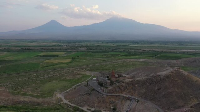 Aerial drone footage flying over the ancient Khor Virap monastery in Armenia. The historic stone complex sits on a hill with the magnificent Mountain in the background.

