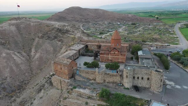 Aerial drone footage flying over the ancient Khor Virap monastery in Armenia. The historic stone complex sits on a hill with the magnificent Mountain in the background.

