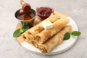 Tasty rolled crepes with honey, jam, butter and mint leaves served on light grey table, closeup © New Africa