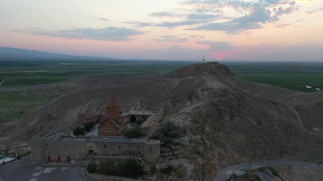 Aerial drone footage flying over the ancient Khor Virap monastery in Armenia. The historic stone complex sits on a hill with the magnificent Mountain in the background.

