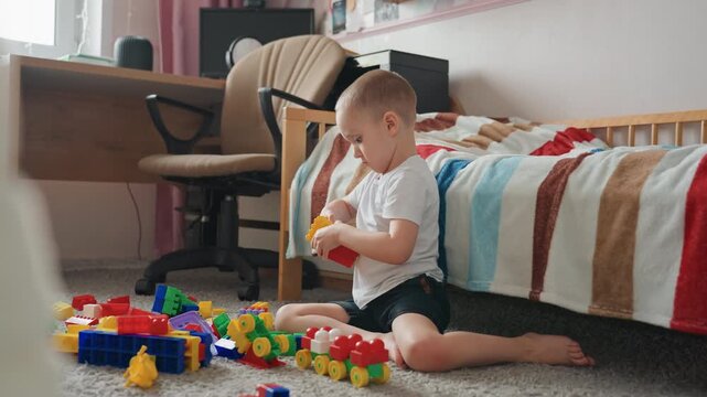 White boy building tall block tower on carpet by bed, focused hands assembling colorful pieces, roleplaying little builder with concentrated expression, creative early learning and quiet constructive