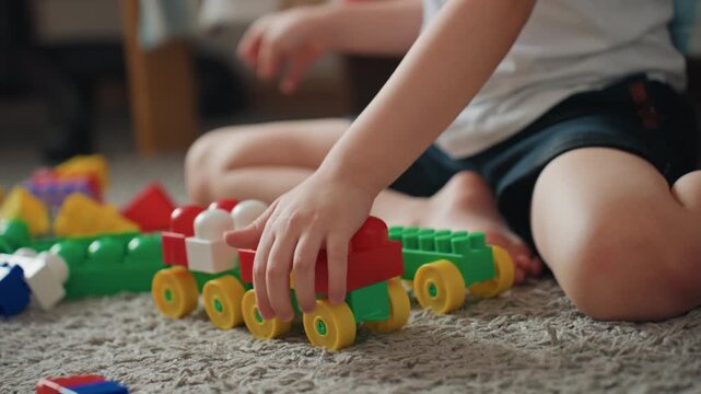 White boy assembling colorful toy train on carpet, closeup of hands and wheels, fine motor practice and tactile exploration, playful little engineer role in cozy bedroom setting, focused constructive
